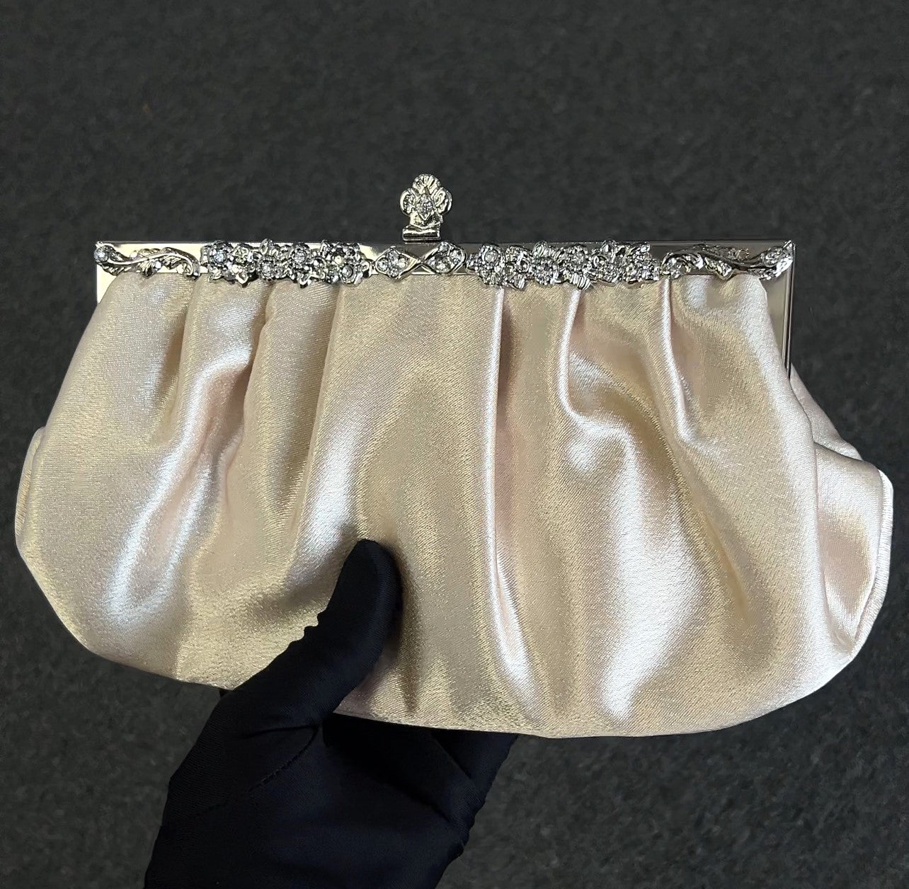 Gold clutch with decorative frame held Timeless, romantic, and endlessly elegant. This champagne-toned satin clutch features soft, delicate ruching that catches the light with a subtle, luxurious sheen. It is the perfect accessory for the woman who values classic sophistication over trends