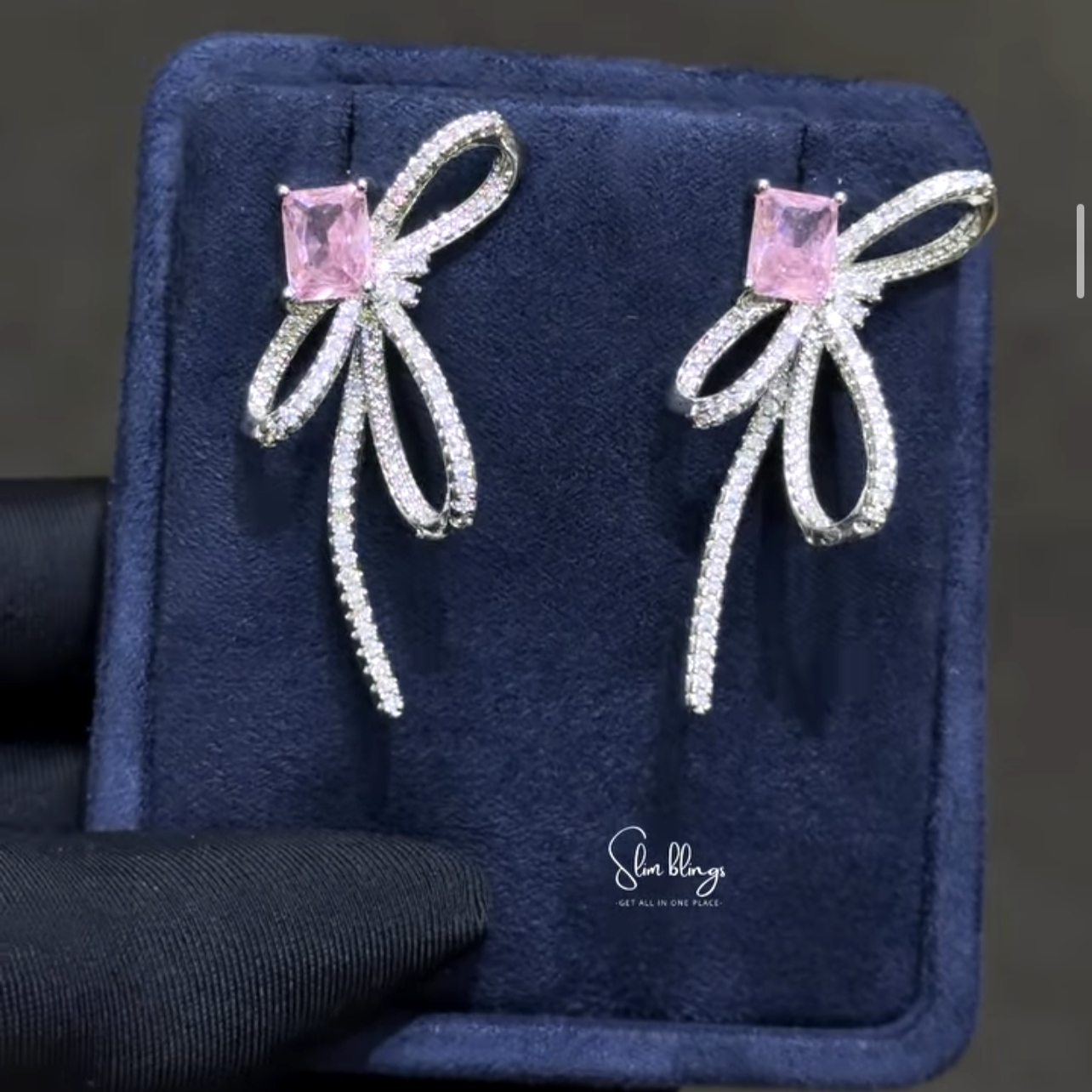Bow-shaped earrings with pink gemstones. Crafted with extended ribbon streamers that drape elegantly, catching attention with every tilt of the head.
