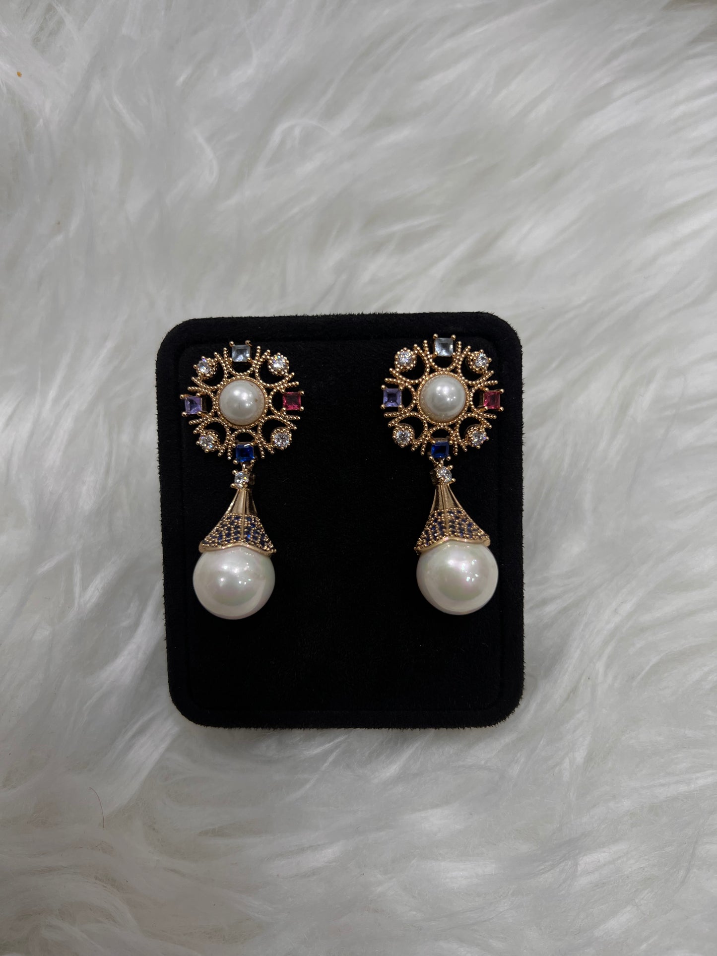 Suspended below is a dramatic, large teardrop-shaped pearl capped in a beautifully textured gold cone encrusted with brilliant royal blue micro-crystals.