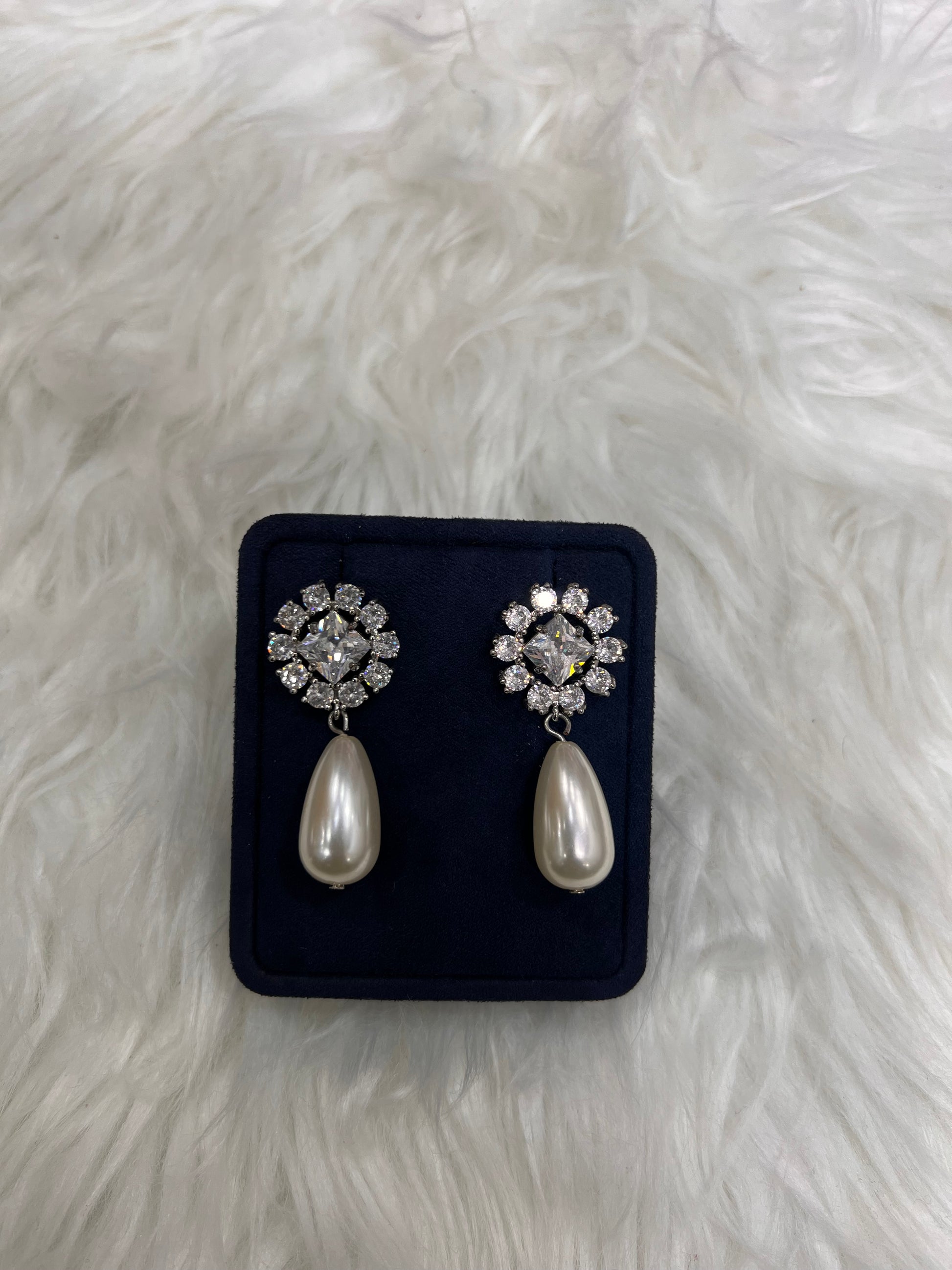 A pair of silver-toned statement earrings with clear crystal floral clusters and teardrop pearl drops, They are the quintessential choice for brides, bridesmaids, or anyone seeking to elevate a formal gown with effortless sophistication.
