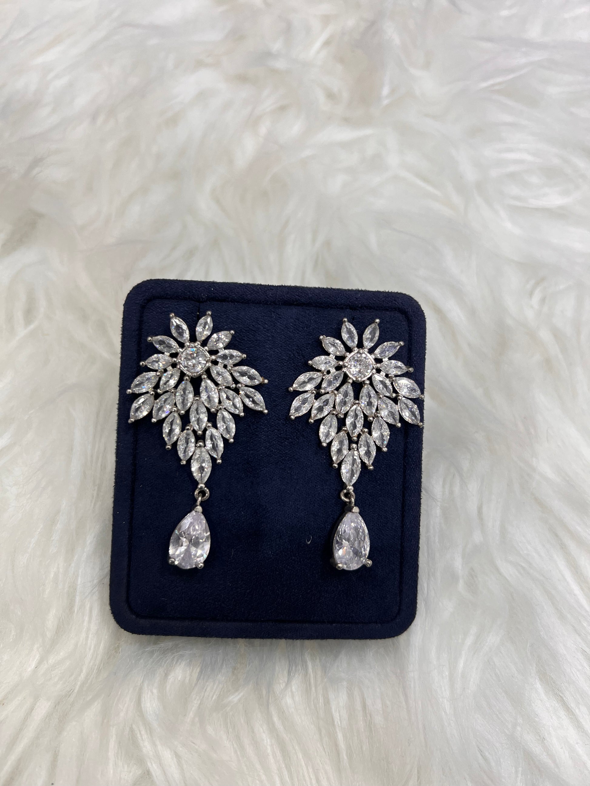 A pair of silver-toned floral drop earrings with clear crystal-like stones,  Perfect for the bride who wants a high-glamour, timeless red-carpet look on her special day.