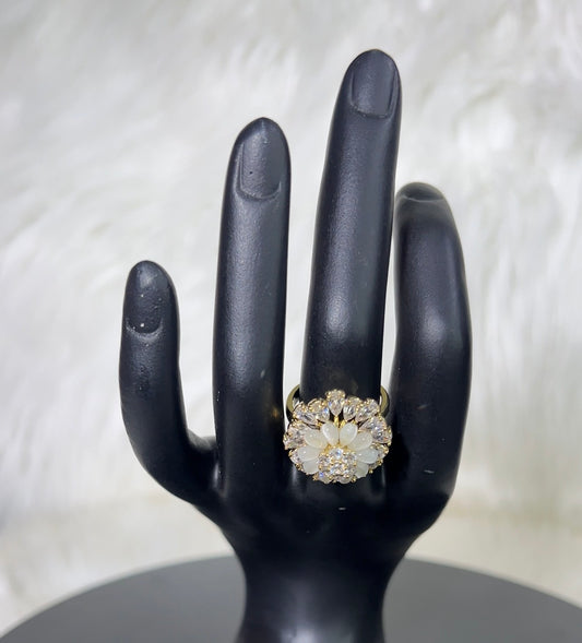 A gold ring with a large white floral cluster center and small clear stones