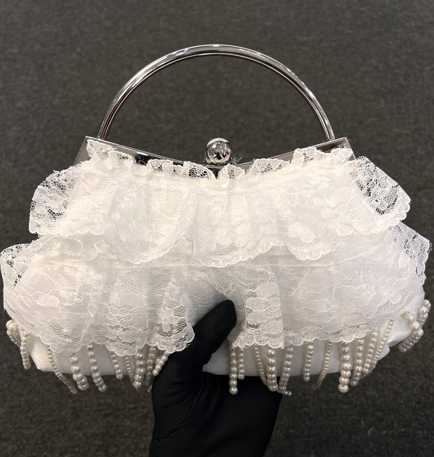 A white lace and ruffle evening clutch bag with pearl fringe, a silver metal frame, and a clear acrylic top frame 