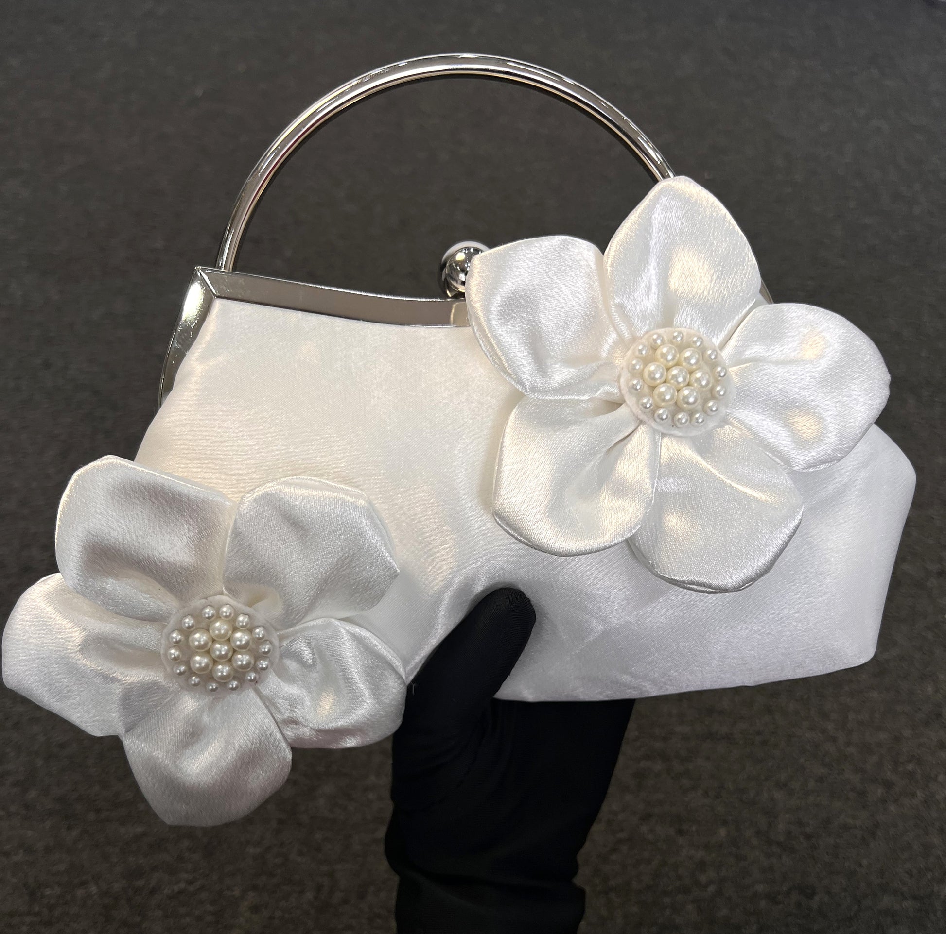 A white satin evening clutch bag with large fabric flower appliqués and pearl-like floral centers