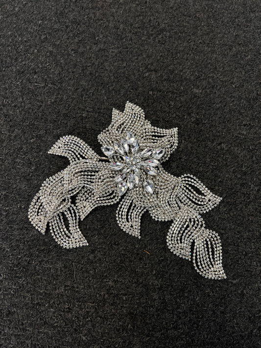 A silver rhinestone hair accessory with a floral and leaf design, featuring a central clear crystal flower. Lightweight frame structured to sit securely against structured hairstyles, up-dos, or sleek low buns.