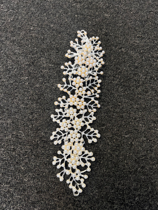 A decorative white lace applique trim with small pearl-like beads and gold center accents. Symmetrical shape drapes smoothly along low buns, chignons, or draped across the back of a half-up hairstyle.