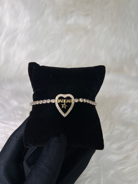 A gold heart-shaped bracelet with clear rhinestones and the word 'JADEAR' on the front,  Plated in warm yellow gold, this bracelet adds designer-inspired flair to evening wear, special events, or high-fashion stacking.