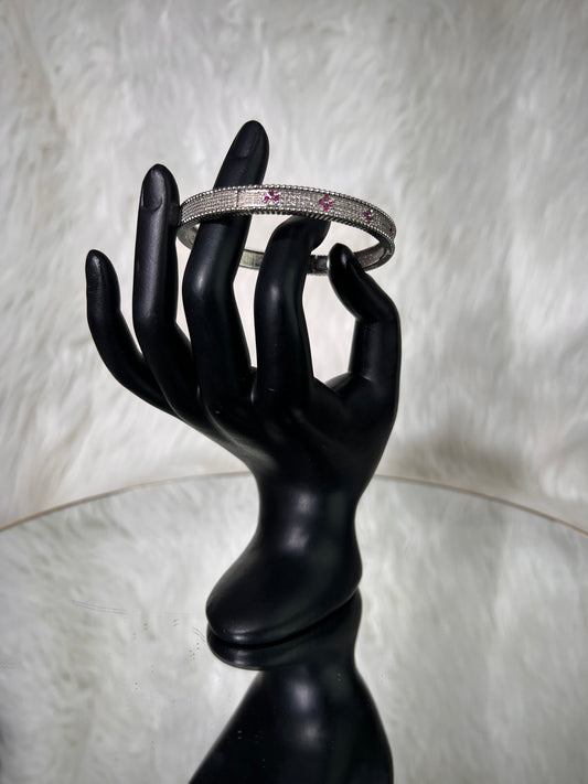 A silver-toned bangle bracelet with small pink gemstones. 