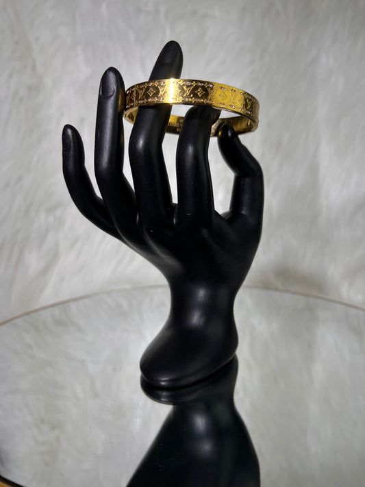 A gold-tone bangle bracelet with an engraved monogram pattern, the polished finish delivers an effortlessly luxurious aesthetic for both daily and stacked wear.