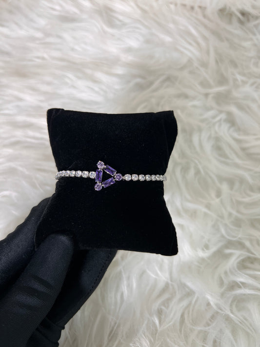 A silver-tone bracelet with a purple triangular gemstone centerpiece and clear stones along the band, 