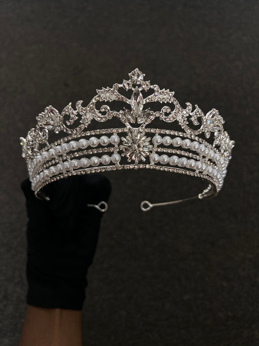 An ornate silver tiara adorned with clear crystals and rows of white faux pearls, Best For: Classic brides, vintage-themed weddings, and high-neck lace bridal gowns.