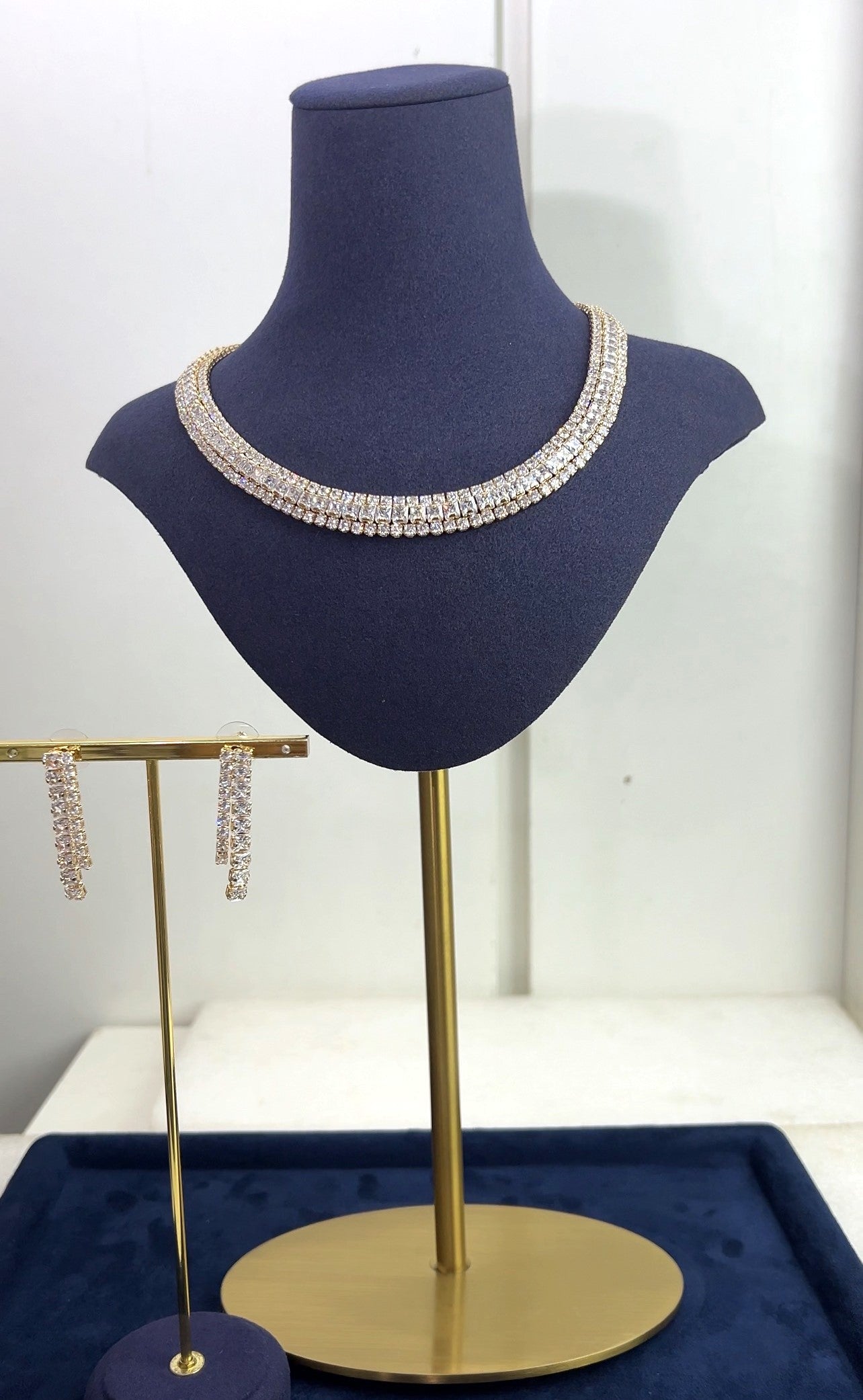 Necklace on a mannequin bust with matching earrings on a stand against a white background