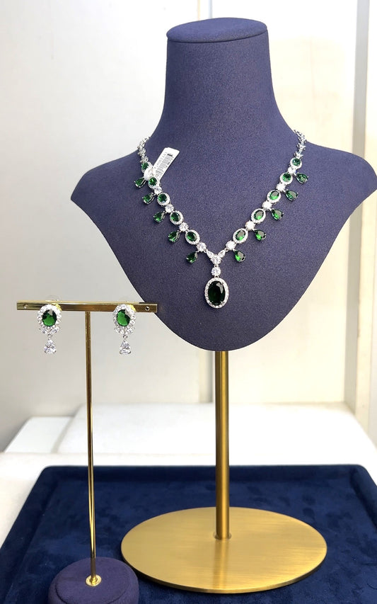 Jewelry set on a mannequin bust with green and clear gemstones on a white background