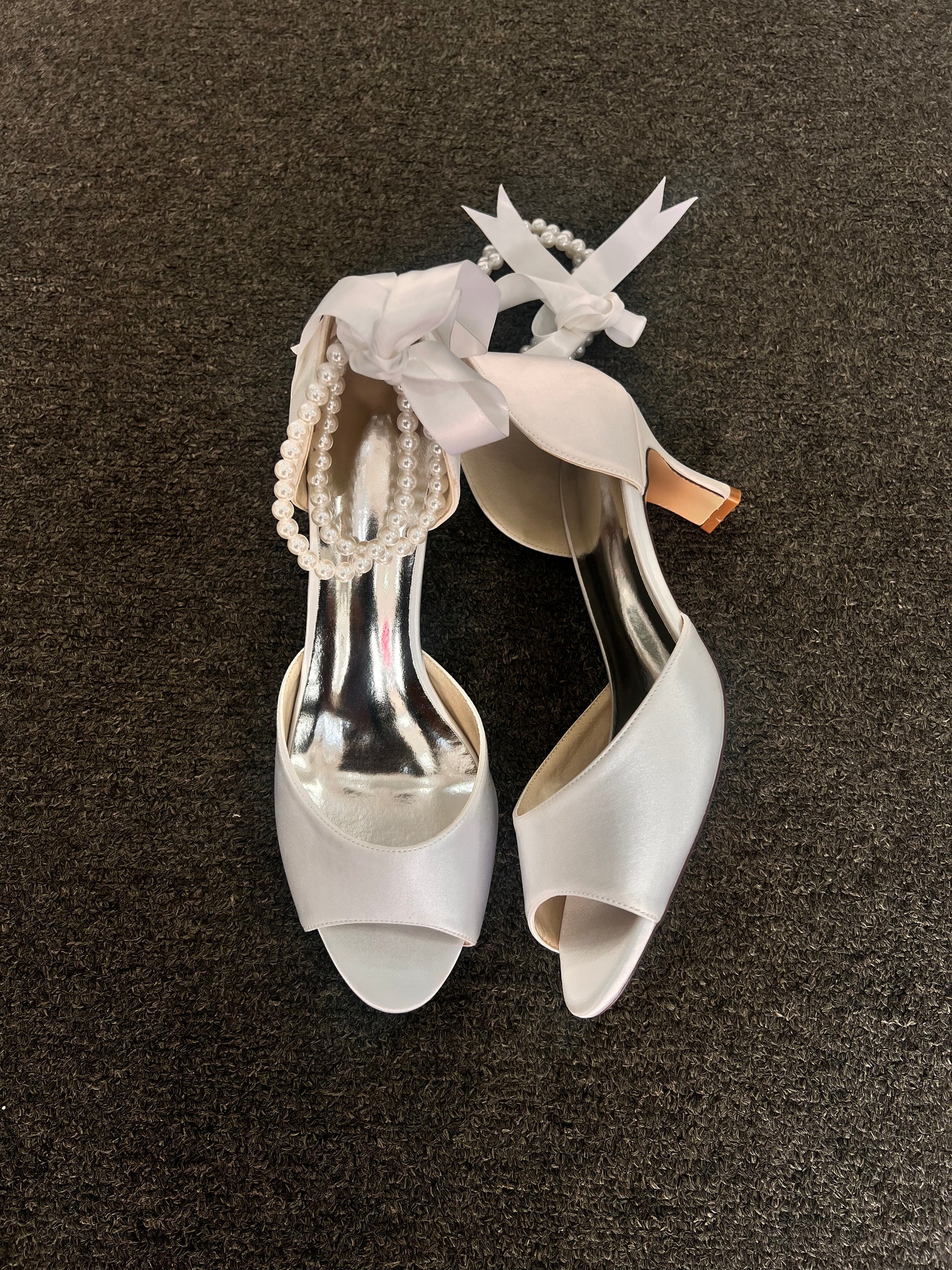 The standout feature is the exquisite ankle wrap, which combines a delicate pearl strand with a luxurious satin ribbon tie for a customizable, secure fit.