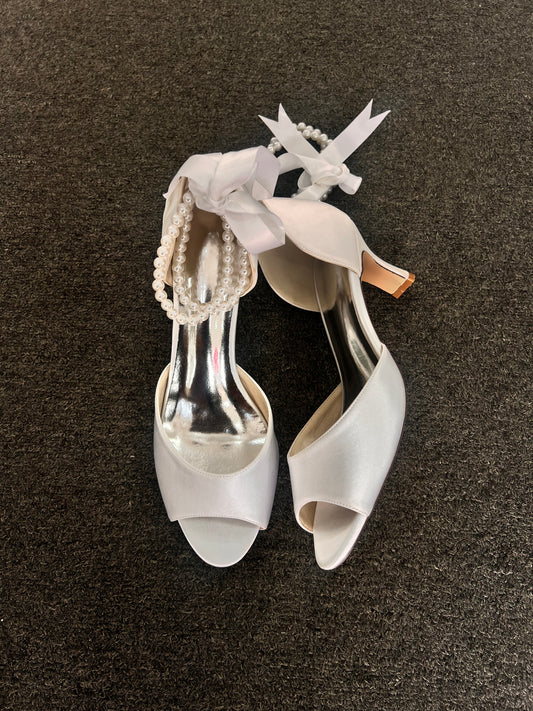 The standout feature is the exquisite ankle wrap, which combines a delicate pearl strand with a luxurious satin ribbon tie for a customizable, secure fit.
