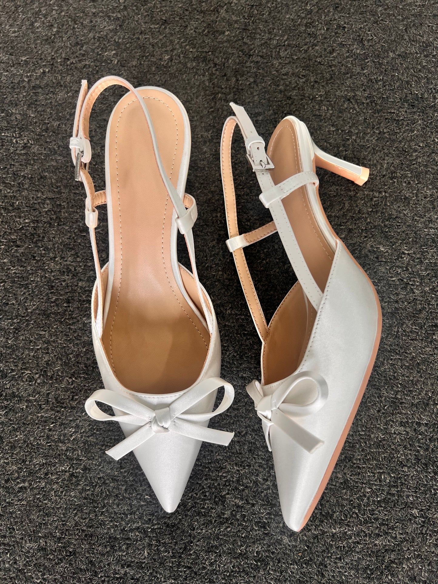 Pair of white high-heeled shoes with bow. The slender kitten heel and adjustable slingback strap provide a refined lift without compromising on stability, making them an ideal choice for long days and celebratory evenings.