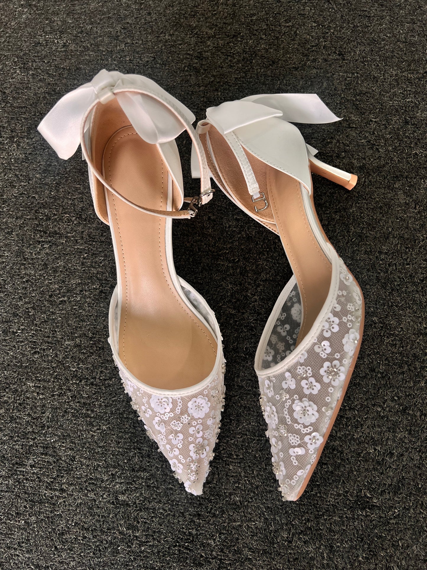 Pair of white wedding shoes with lace detailing . The design is beautifully balanced by a smooth satin heel and an oversized satin bow at the back, adding a dramatic yet feminine finishing touch.