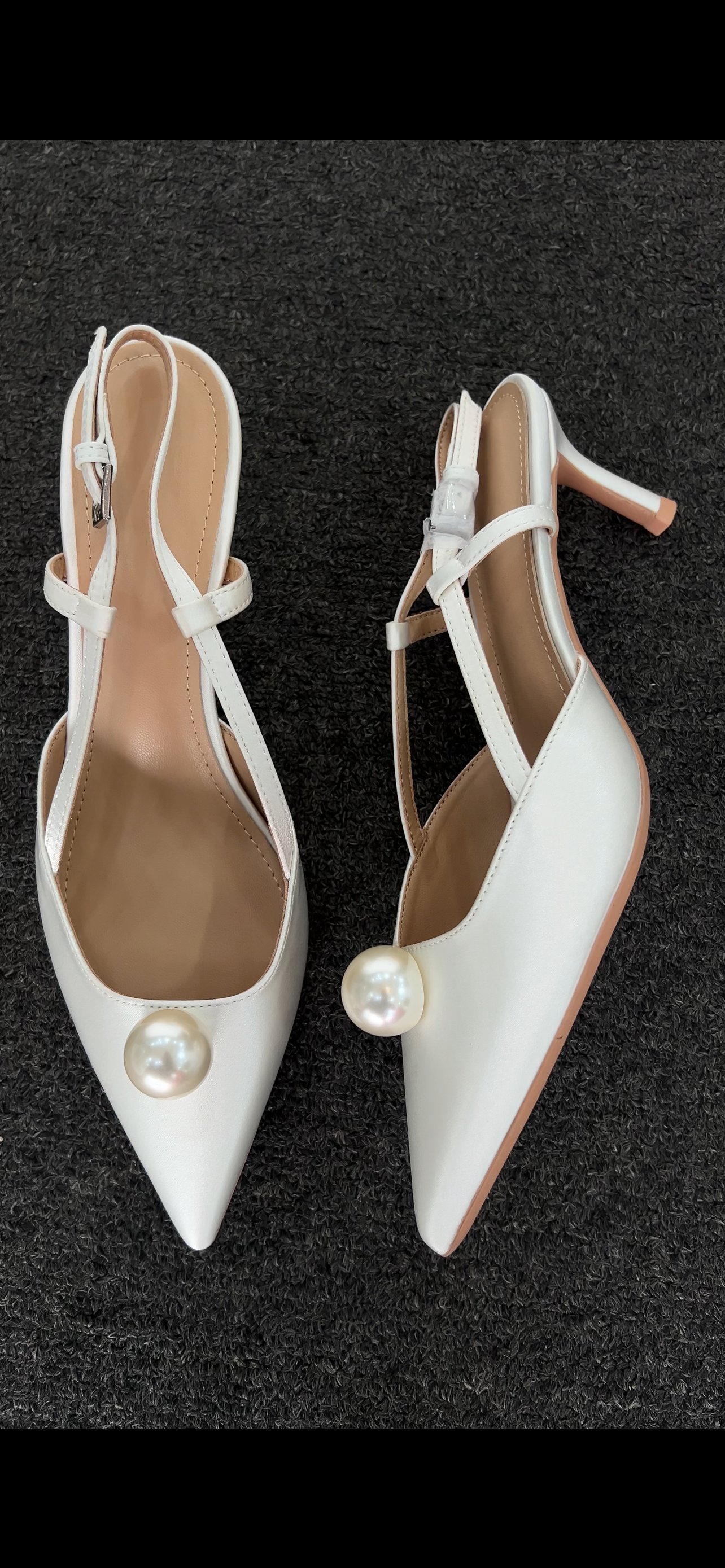 Pair of white high-heeled shoes with pearl embellishments . he standout feature is the exquisite ankle wrap, combining a lustrous pearl strand with a soft satin ribbon tie