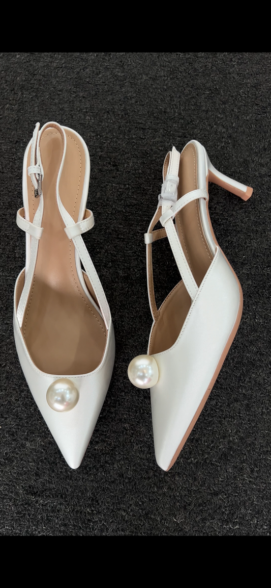 Pair of white high-heeled shoes with pearl embellishments . he standout feature is the exquisite ankle wrap, combining a lustrous pearl strand with a soft satin ribbon tie