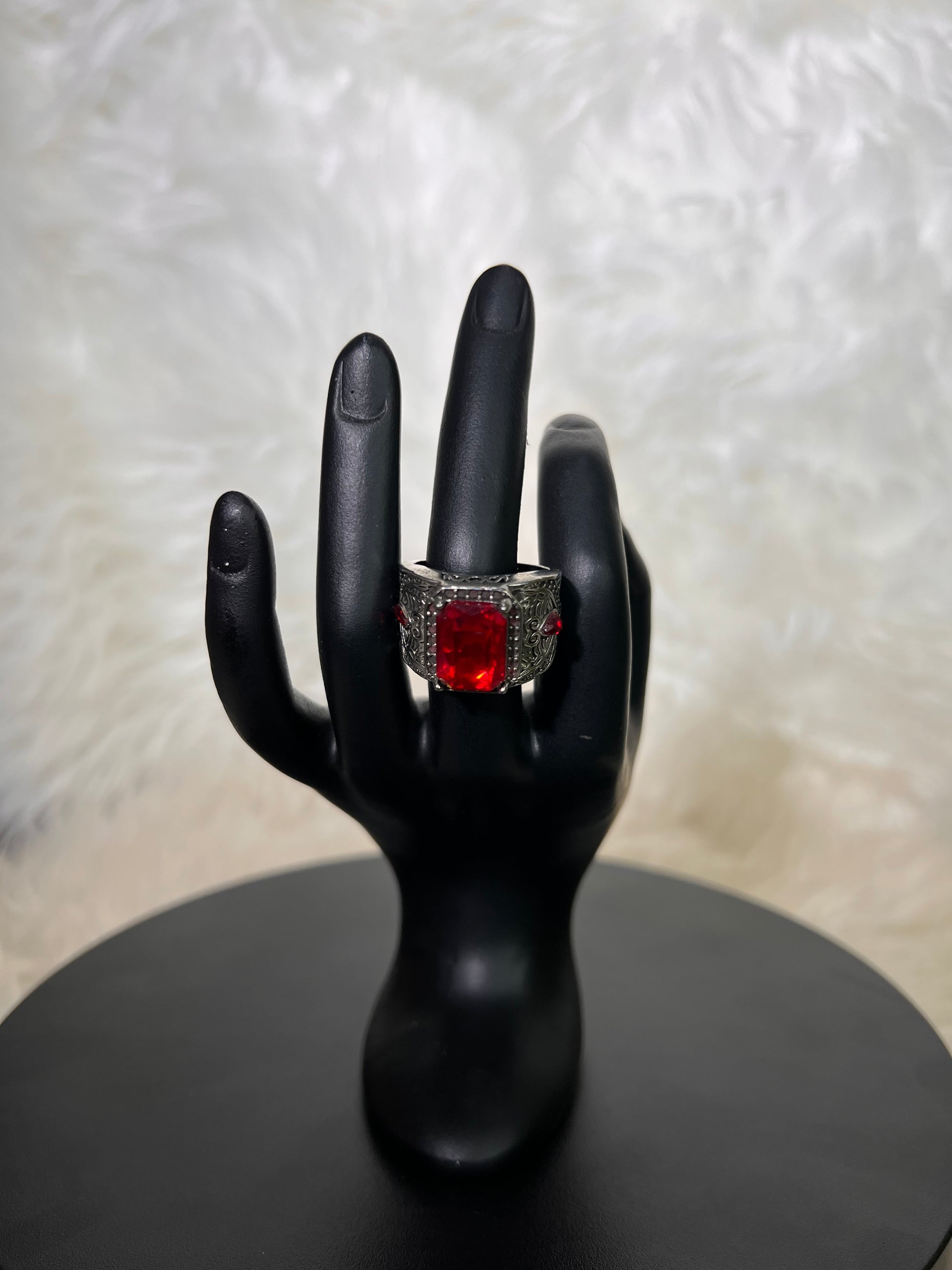 A magnificent, emerald-cut ruby-red center stone nestled within a wide, antique-engraved silver band. Accented with subtle side jewels, it exudes a regal, vintage-inspired majesty.